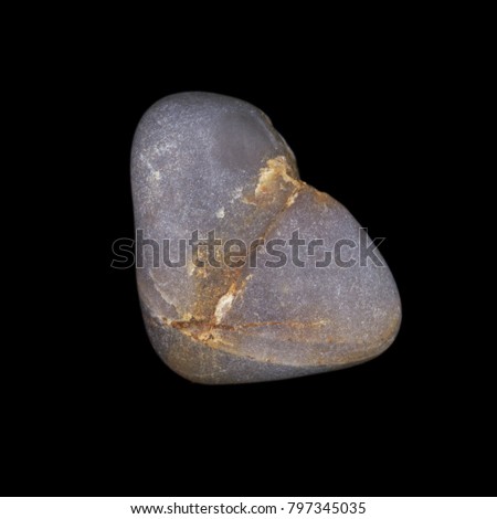 A high resolution macro close up of a grey pebble or stone with yellow striations isolated against a black background