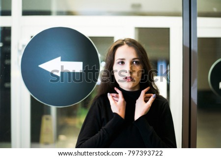 young asian girl walking in the night city . Cute woman stand near closed door and signboard with arrow  to entrance. business building or shop window, showcase of mall