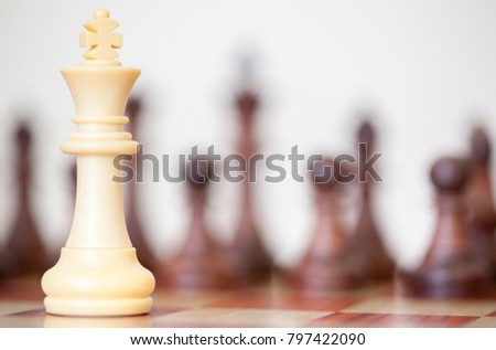 White king on a chess board alone against all black pieces. White king fights against black enemy team on board.