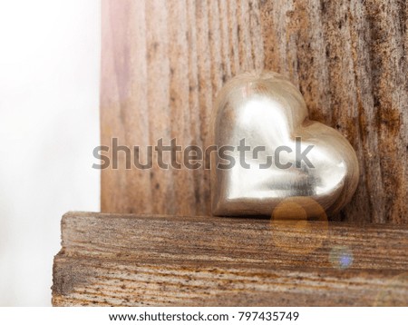 Silver, metal heart on background of light wooden wall of country house; close-up; with copy space