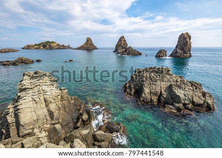View on the rocky islands in Aci Trezza, Sicily, Italy, with the Islands of the Cyclops in the background. Royalty-Free Stock Photo #797441548
