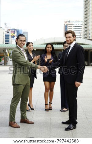 Two business man handshake with team in background  and city view. Two businessmen shaking hands with cityscape in background. Two businessmen shaking hand and modern buildings in the background
