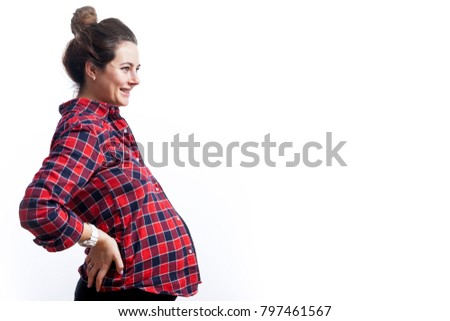 Young dark-haired woman at 37 weeks gestation in black dress and plaid shirt smiles and holds on to the back on isolated white background, side view