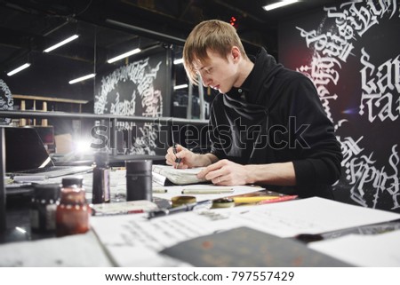 Portrait of a master calligrapher. A tattoo artist makes a sketch while sitting at a table in the Studio