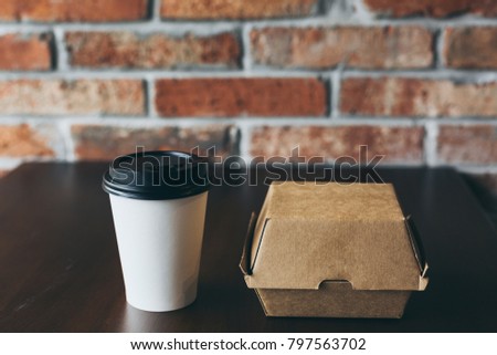 A paper box and a coffee cup for breakfast on a wooden table near a brick wall. Street food in a box and a cup of coffee.