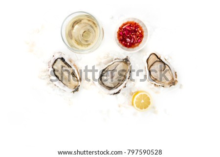 An overhead photo of three freshly opened oysters on ice, with a glass of wine, lemon, the typical vinaigrette sauce, and a place for text