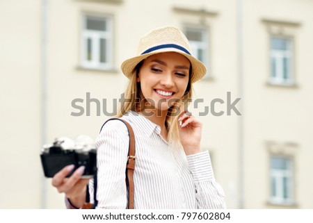 Beautiful Happy Girl Taking Photos On Camera. Happy Smiling Young Woman In Stylish Shirt And Hat Making Selfie Photo While Walking Outdoors. Travel Concept. High Resolution.