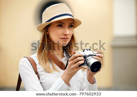 Tourist Girl With Camera Taking Photos On Street. Portrait Of Beautiful Woman In Stylish Clothes And Hat Holding Camera In Hands And Making Photo Outdoors. High Quality Image.