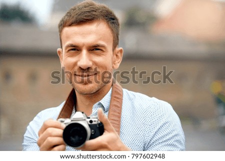 Male Photographer Taking Photos On Camera On Street. Close Up Portrait Of Happy Young Man In Shirt Using Camera, Making Photos During His Travel. High Resolution.
