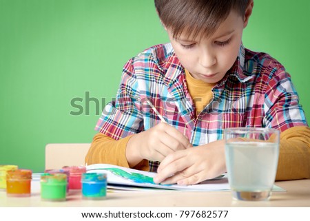 Caucasian boy is intently painting with gouache.