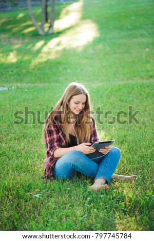 Young woman using tablet outdoor sitting on grass, smiling.