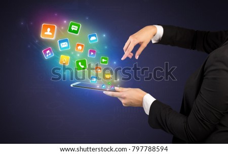 Hand holding tablet and application icons falling inwards
