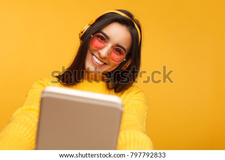 Cheerful young hispanic woman taking a selfie on yellow background. Colorful portrait of girl smiling and making a picture of herself