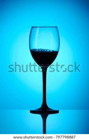 colorful drink with splash in wineglass on blue background with reflection