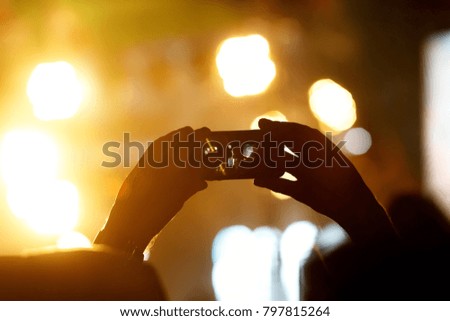 Silhouette of hands using camera phone to take pictures and videos at live concert, smartphone records live music festival.
