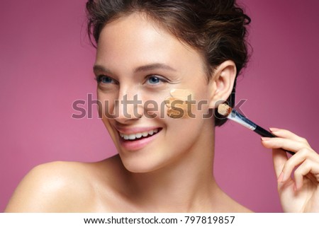 Beautiful woman with tone cream lines on her face. Photo of smiling brunette woman with healthy skin and perfect makeup on pink background. Skin care concept