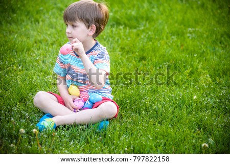 Little boy hunting for Easter egg in spring garden on Easter day. Cute child sit on grass with eggs in his hands. traditional bunny celebrating feast