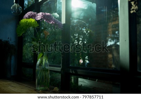 Purple and green flowers in glass bottle on wooden table, soft focus