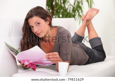 young woman lying down on a couch is reading a magazine