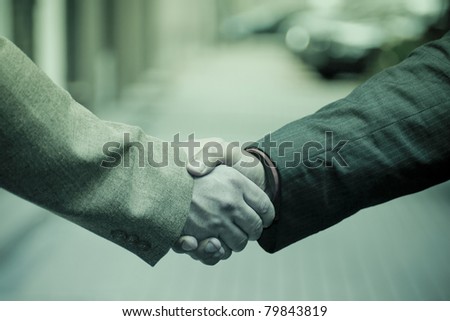 Closeup picture of businesspeople shaking hands, making an agreement. Against pavement. Blue mood.