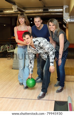 Man prepares throw  ball in bowling club and friends him encourage , focus on fellow in center