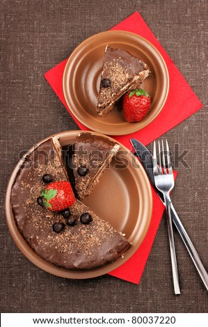Two plates with homemade chocolate cake, fork and knife on brown canvas.
