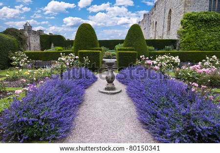 a gravel pathway between formal beds of lavender leading to an old sundial and trimmed hedges beyond. Horizontal format. Royalty-Free Stock Photo #80150341