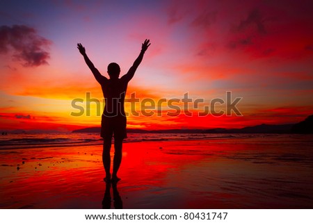 Young man doing exercises standing on wet sand at bright sunset background