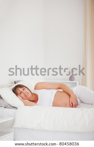 Good looking pregnant woman relaxing while lying on her bed in her apartment