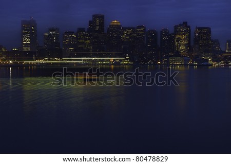 View across Boston Harbor with lights from water taxi and other boats streaked across foreground. Horizontal shot.