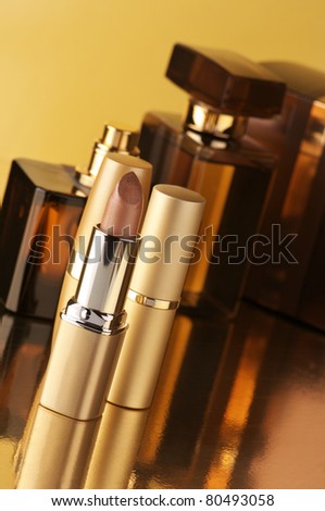 Set of perfumes and lipsticks on gold background.
