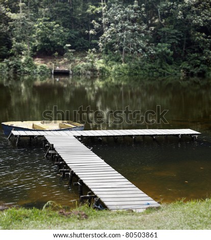 A yellow rowing boat docked by a timber jetty in a rural creek surrounded by green tropical rainforest.