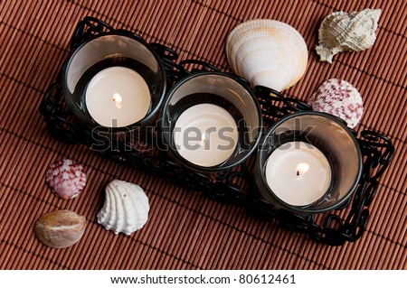 three tea candles with seashells on a dark background