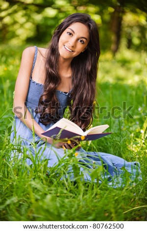 portrait of beautiful young long-haired brunette woman in dress holding book and smiling in park