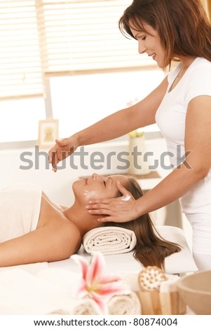 Masseur applying cream on young woman's face in spa.?