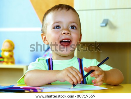 Smiling boy draws with crayons