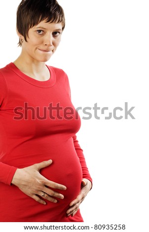 Pregnant young woman in a red shirt comes from the left side into the picture holding her belly. Studio shot against a white background.