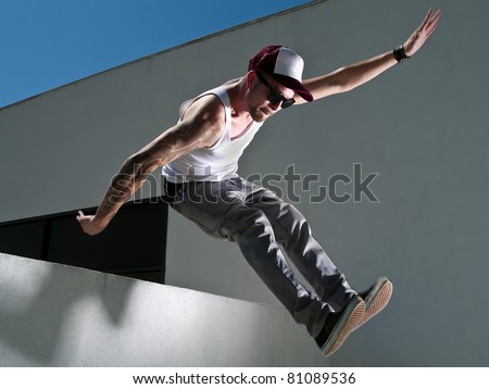 tattooed male parkour free runner jumping off a building Royalty-Free Stock Photo #81089536