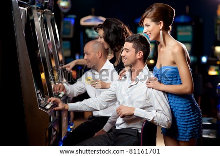 friends enjoying playing the slot machine at the casino Royalty-Free Stock Photo #81161701