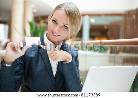 Portrait of a pretty businesswoman sitting at cafe with a laptop using wireless internet, showing business card to camera