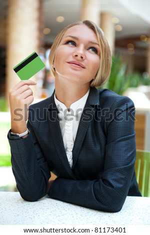 Closeup portrait of cute young business woman smiling while holding credit card and daydreaming