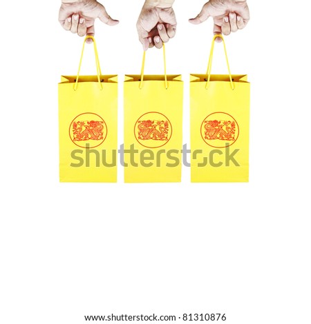 Hand holding on to the handle of yellow color paper shopping bags with exotic oriental dragon design print on its surface, isolated against white.