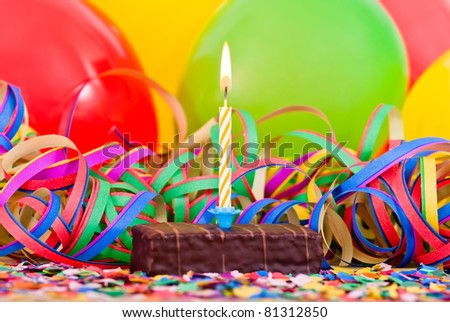 a burning candle on a small cake with streamers and balloons