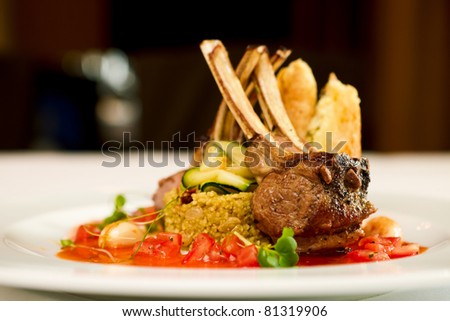 Grilled lamb served on cous-cous with sun dried tomatoes and raisins, goat cheese pastry and smoked tomato and butter sauce Royalty-Free Stock Photo #81319906