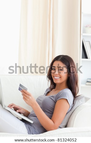 cute woman sitting on sofa in living room holding credit card smiles into camera