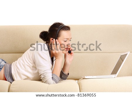 A lying woman on a sofa with a laptop and a headset indoors