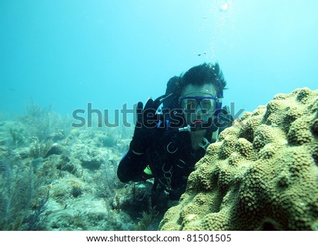 Male scuba diver gives OK sign in shallow brain coral reef in Caribbean