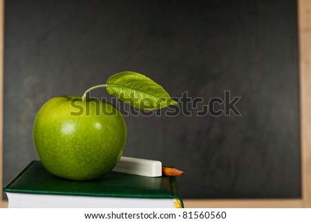 Green apple with leaf against blackboard in class. School concept