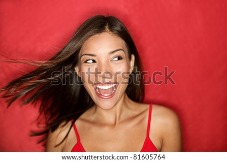 Happy excited woman looking to the side screaming cheerful with wind in the hair on red background. Beautiful multiracial Asian Caucasian female model. Royalty-Free Stock Photo #81605764