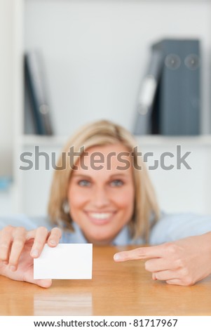 Businesswoman pointing at a card crouching behind her desk in her office